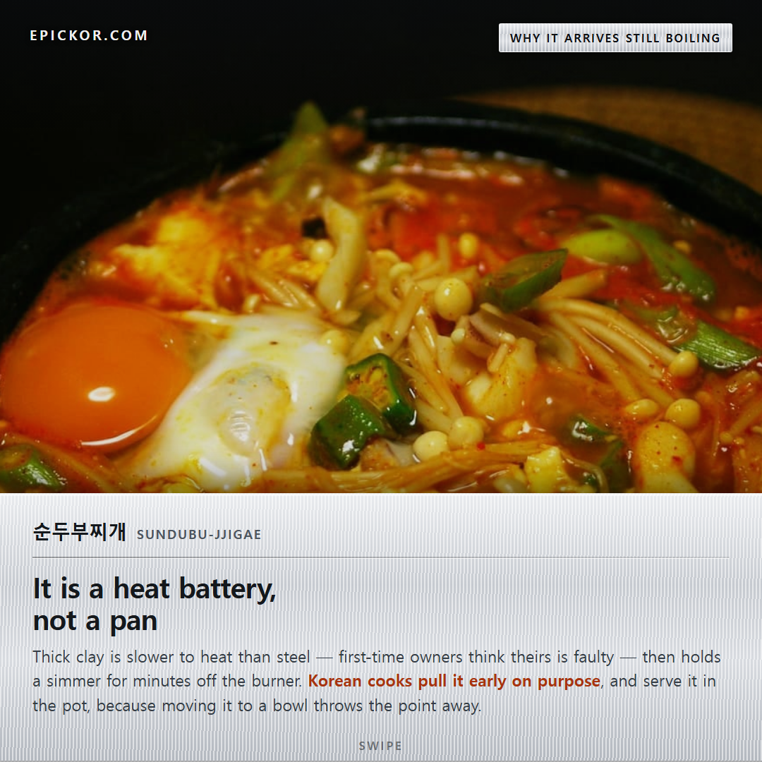 Sundubu-jjigae bubbling hard in a black earthenware pot with a raw egg dropped in at the table