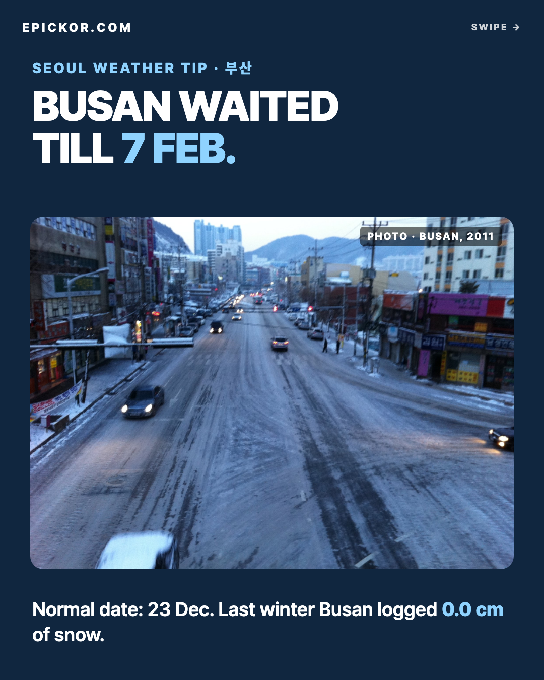 A wide street in Busan on a snow day (uploaded February 2011) — slush on the road, snow on the pavements and shop awnings, hills behind