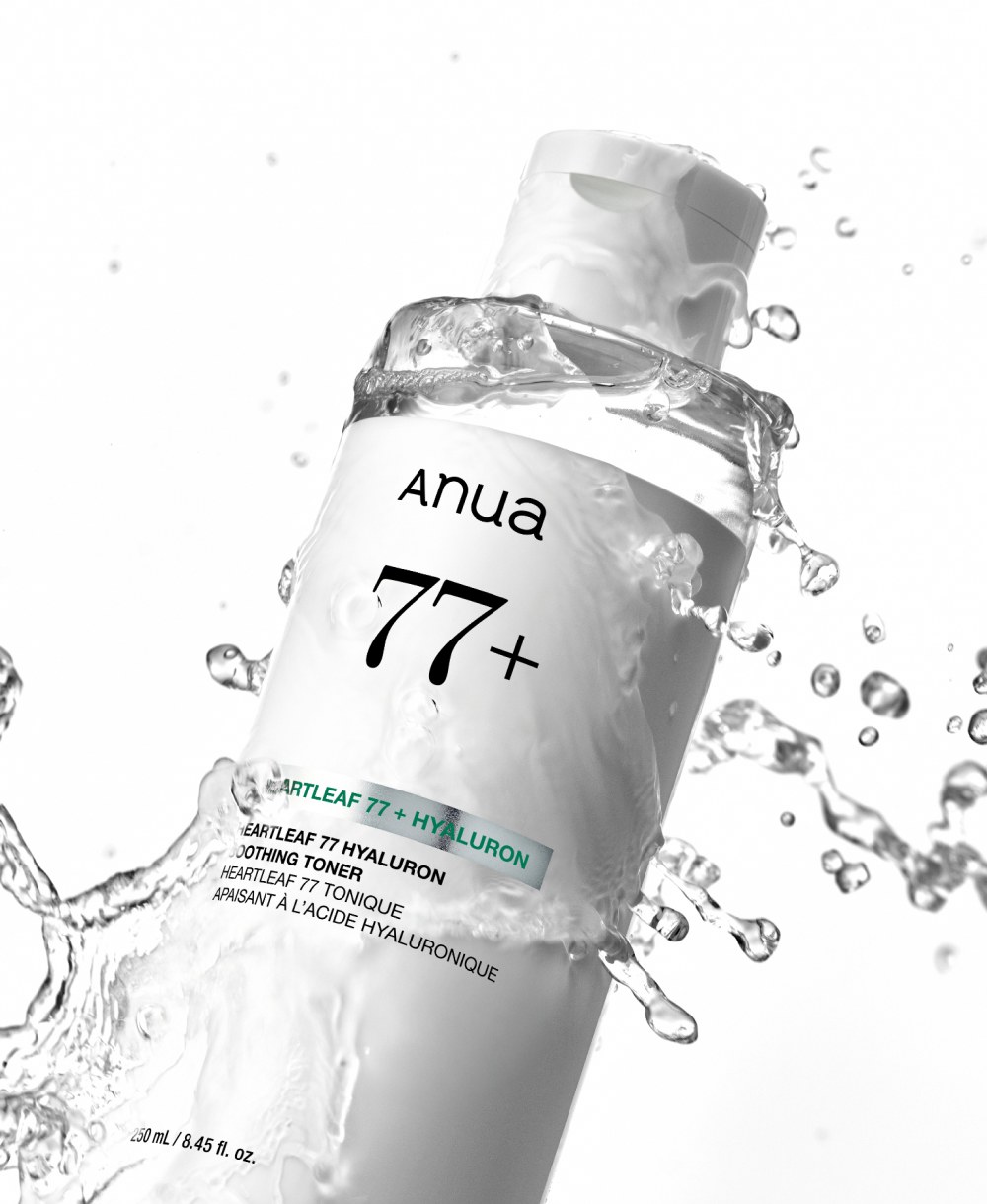 A clear Anua Heartleaf 77+ Hyaluron Soothing Toner bottle, tilted, with water splashing around it against a white background.