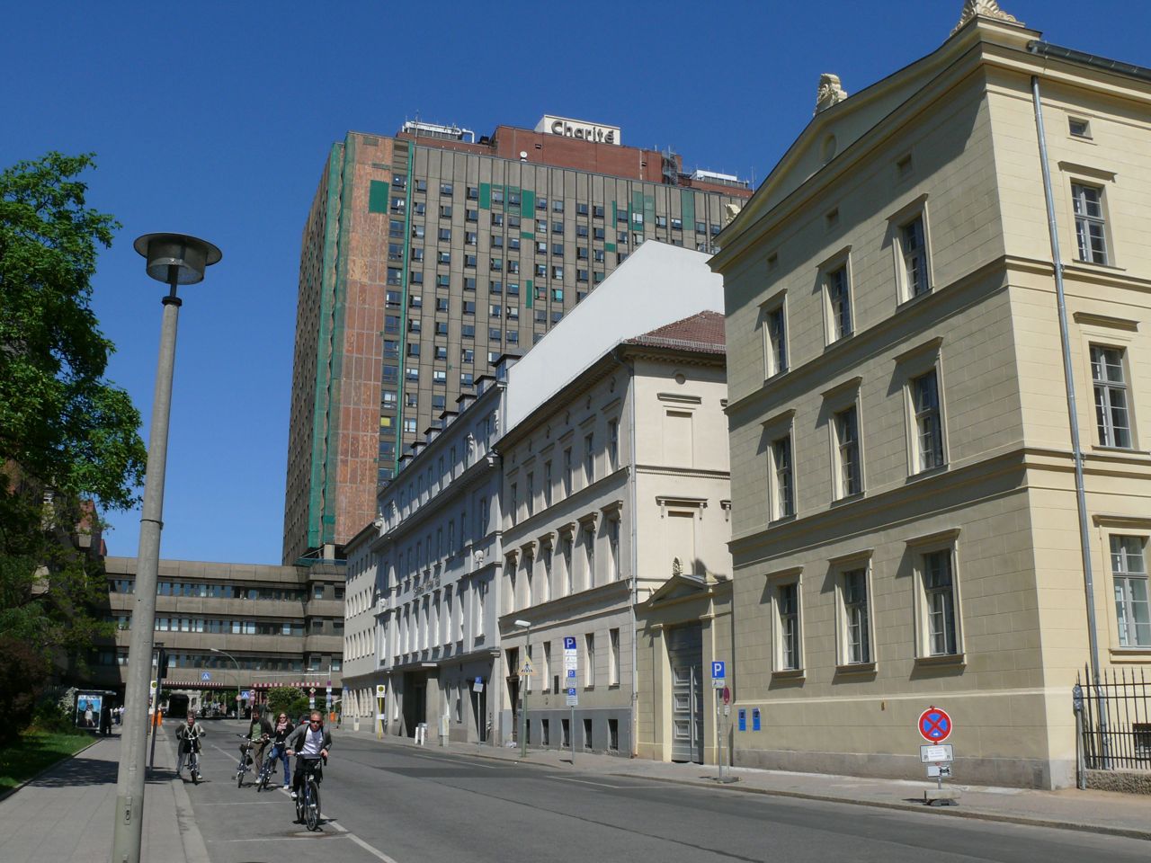 The Charité hospital tower in Berlin-Mitte, with the Charité name on the roof, seen along Luisenstraße with cyclists in the foreground.