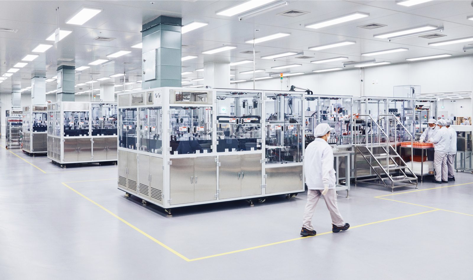 An official COSMAX factory photograph shows automated cosmetics production equipment and operators inside a Korean facility.