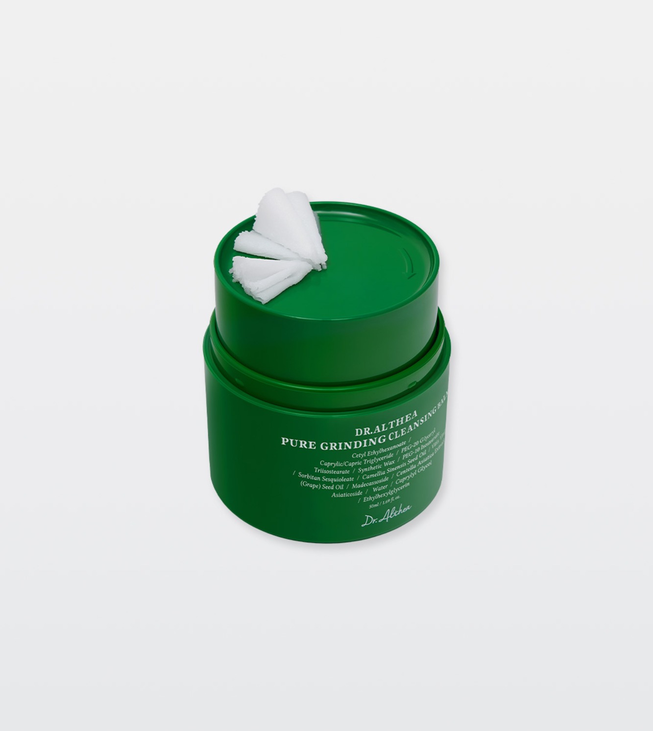 A green Dr.Althea Pure Grinding Cleansing Balm jar with its lid set on top and white balm shavings curled on the lid, on a pale grey background.
