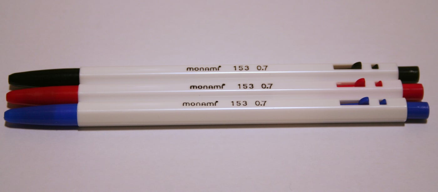 Three Monami 153 ballpoint pens in black, red and blue, the classic white hexagonal barrel design.