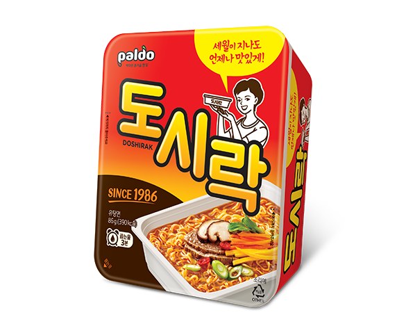 Paldo's official product image of the Korean Doshirak cup: a square red and yellow tray labelled 도시락 DOSHIRAK, with "SINCE 1986", 86g and 390kcal printed on it and an illustration of a woman holding up the tray.