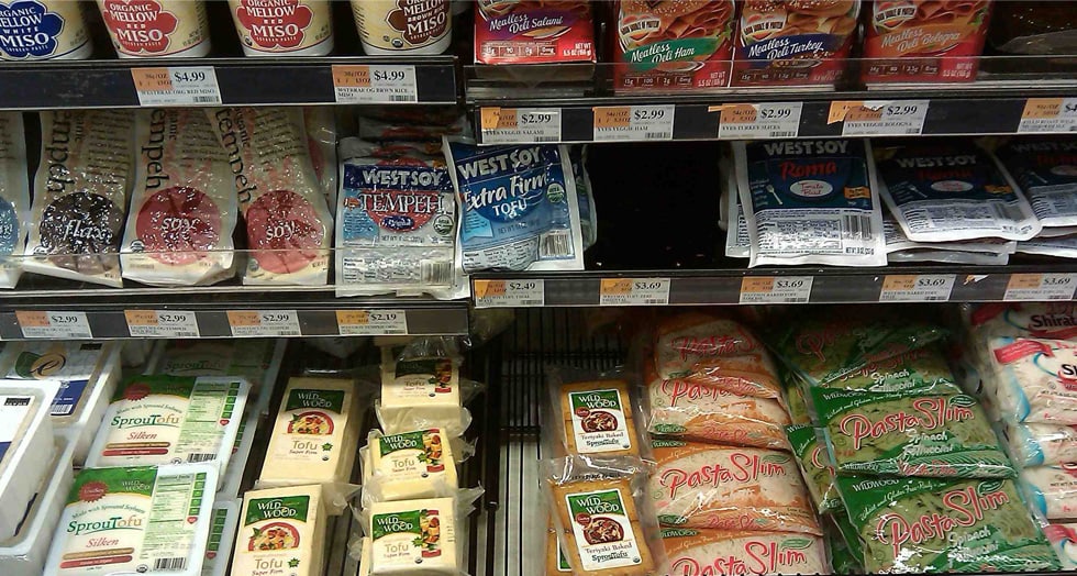 A US supermarket refrigerated case with Wildwood tofu on the shelf, priced in dollars alongside its American competitors.