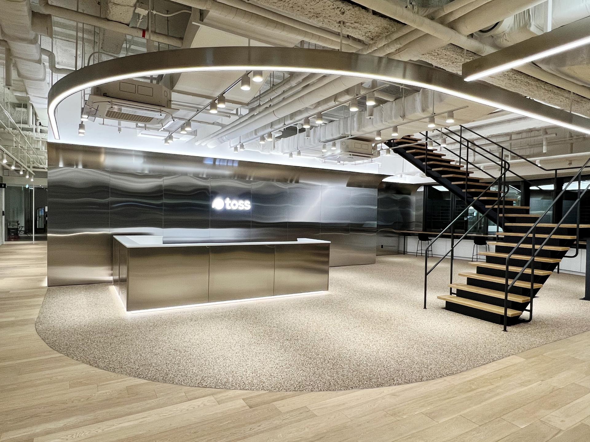 A Toss headquarters staircase and illuminated logo sign show the company's office design beyond the mobile app surface.