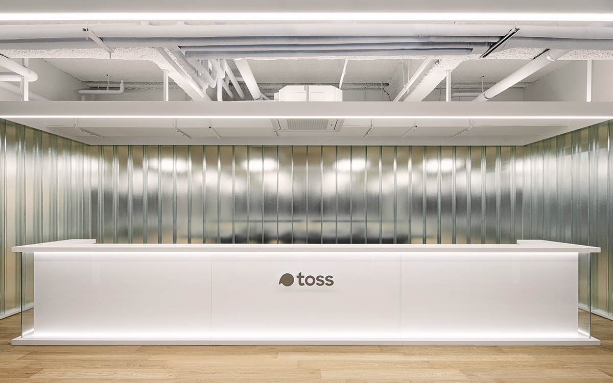 A Toss office reception image shows the company logo on a bright front desk, reinforcing the brand's physical workplace identity.