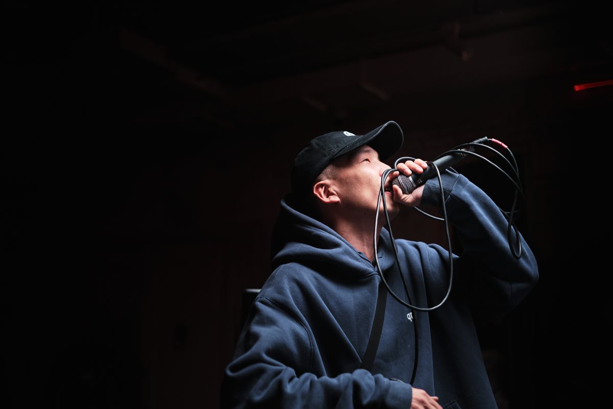 A hoodie-wearing hip-hop performer holding a microphone on a concert stage.