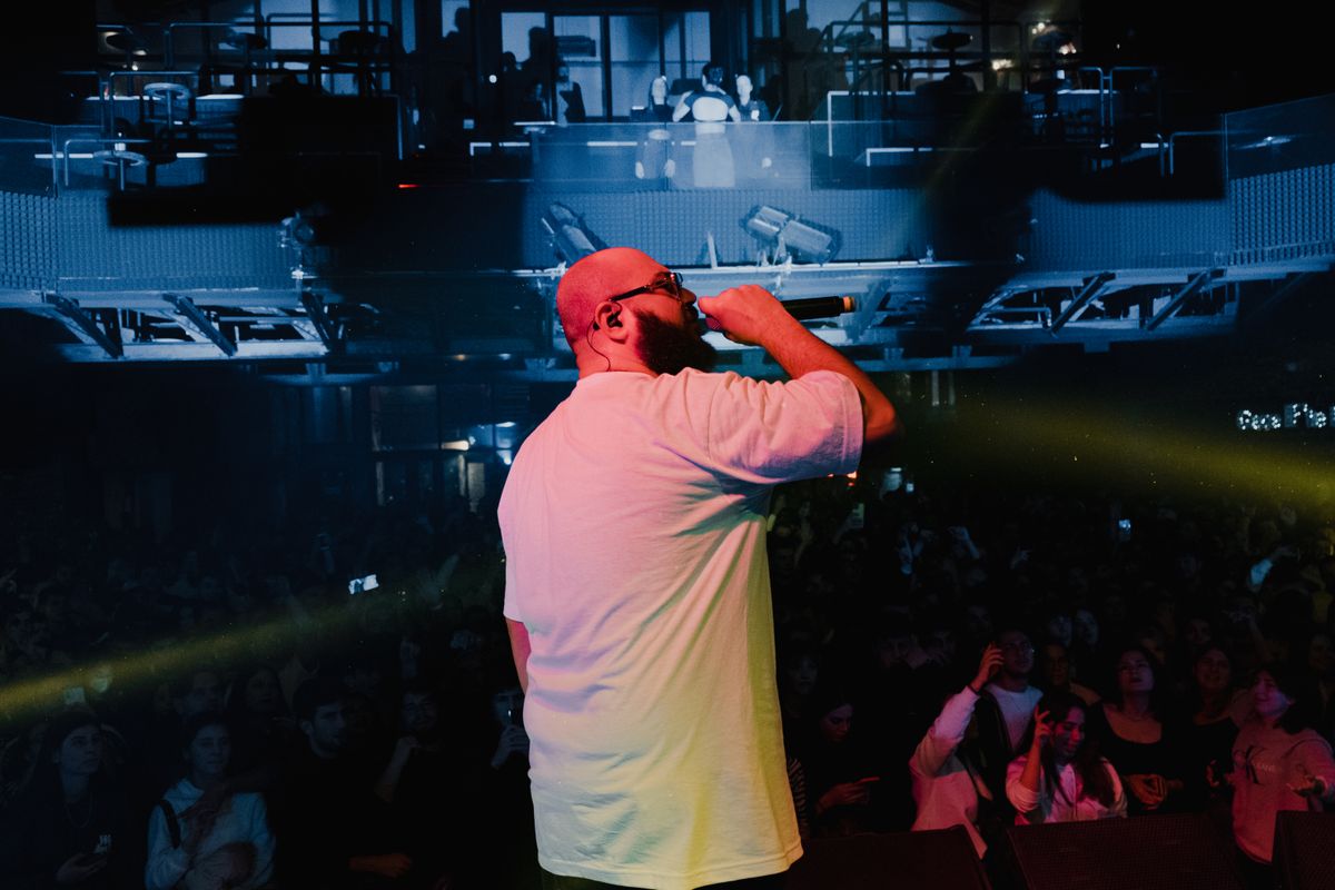 A rapper performing under vivid stage lights during a live concert.