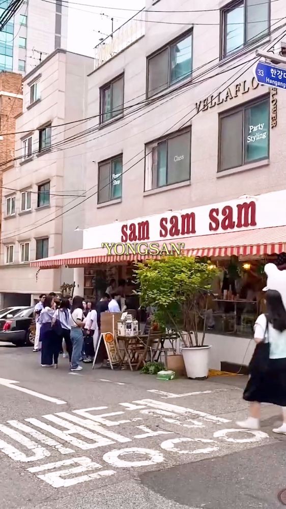 Sam Sam Sam restaurant on a corner in Yongridan-gil, Yongsan, Seoul, with a red striped awning and a crowd waiting outside.