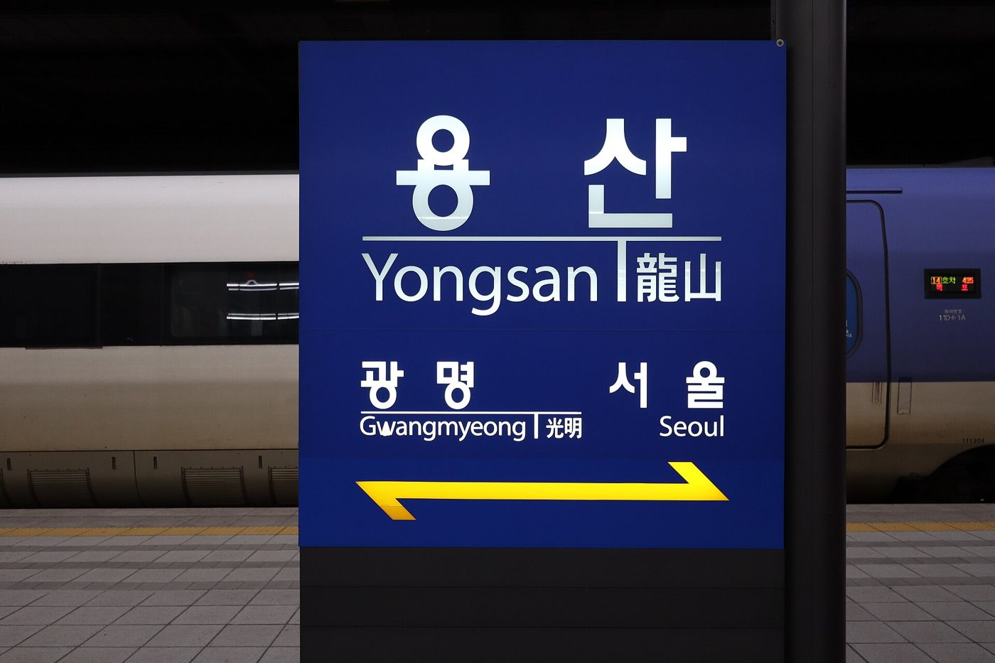 The platform sign at Yongsan Station in Seoul, reading 용산 Yongsan 龍山 with Gwangmyeong and Seoul as the next stops, and a KTX train standing behind it.