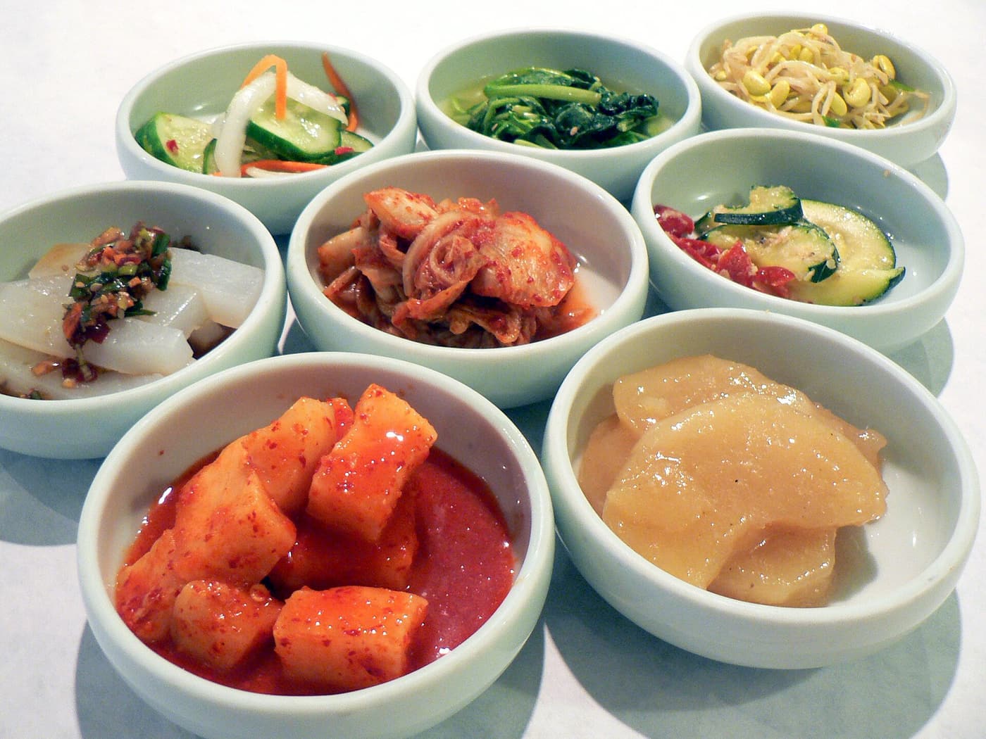 Seven small bowls of banchan including napa kimchi, kkakdugi, bean sprouts and spinach.