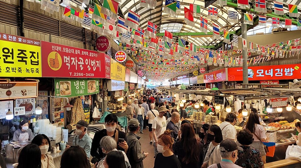 The covered main aisle of Gwangjang Market in Seoul, filled with food stalls and shoppers