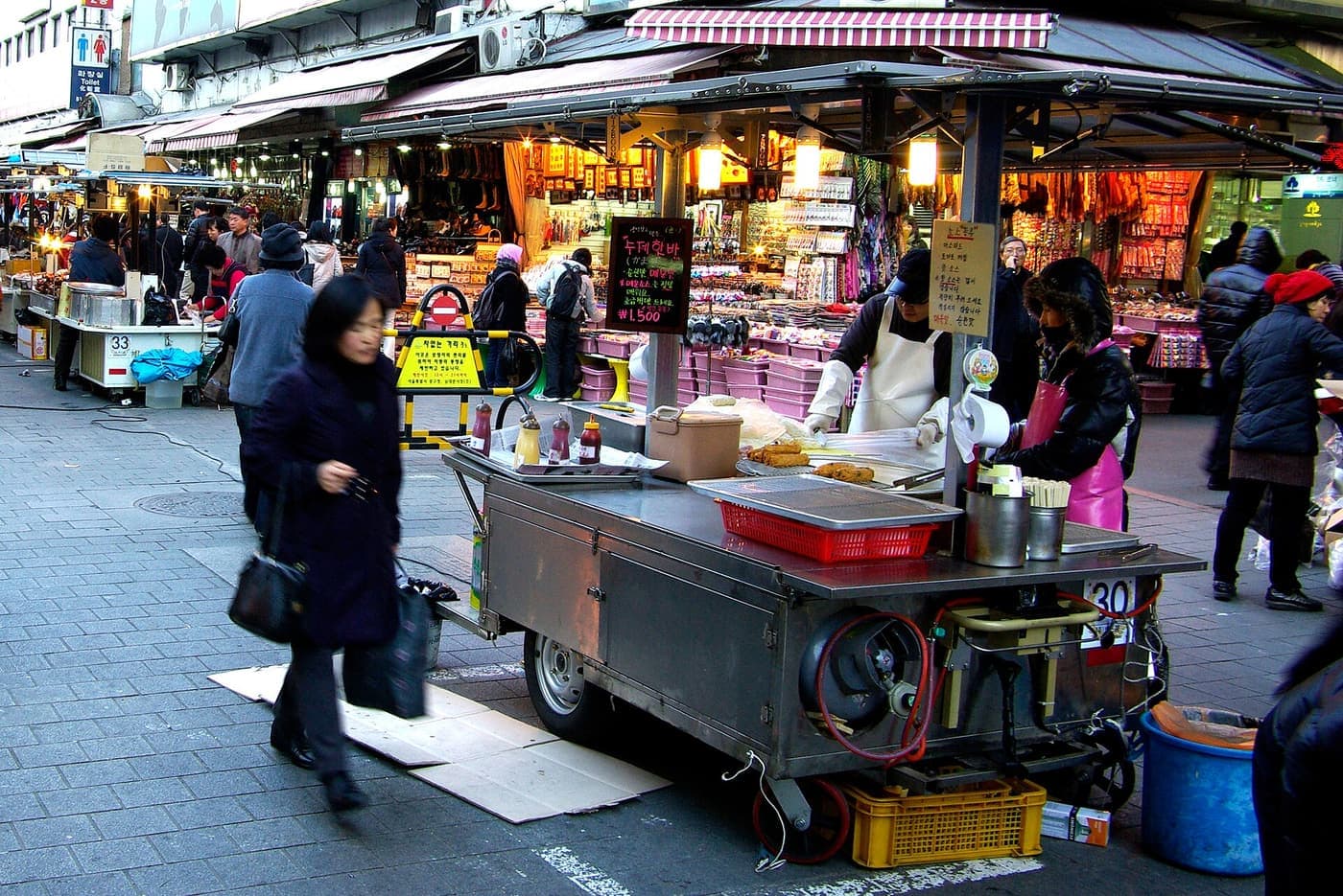 A street food cart on a Seoul shopping street, a vendor cooking behind a steel counter.
