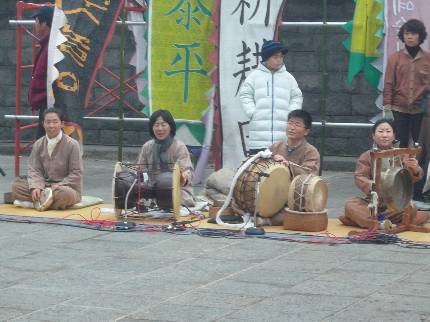 A Korean nongak ensemble performing with drums and gongs outdoors.