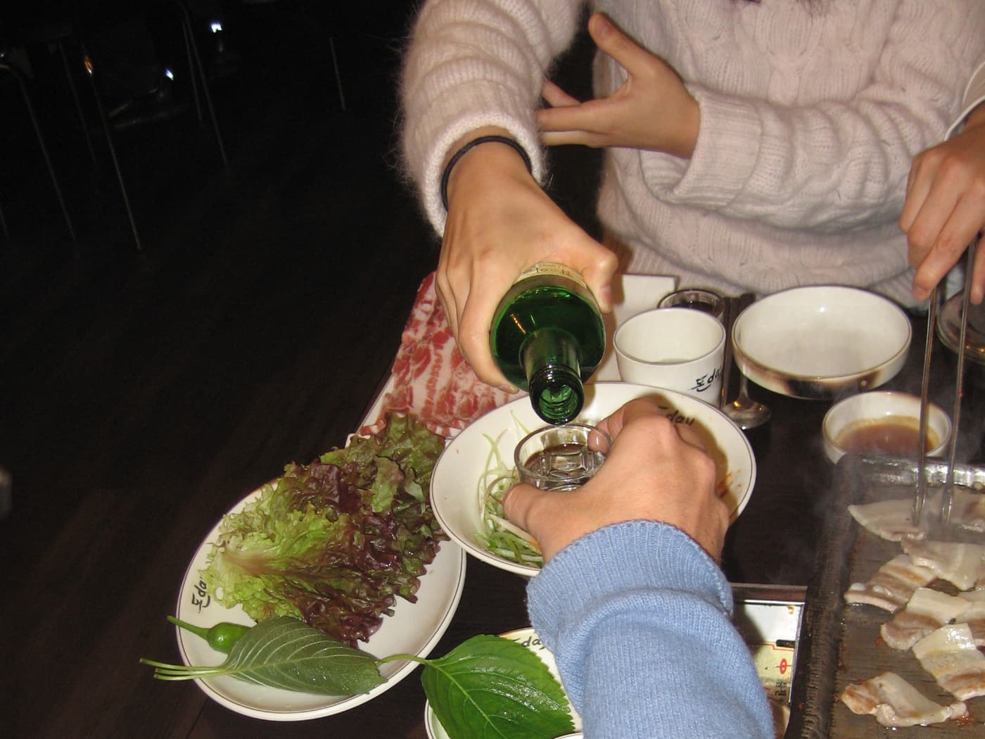 A Korean drinking table with soju glasses, side dishes and shared plates in the middle.