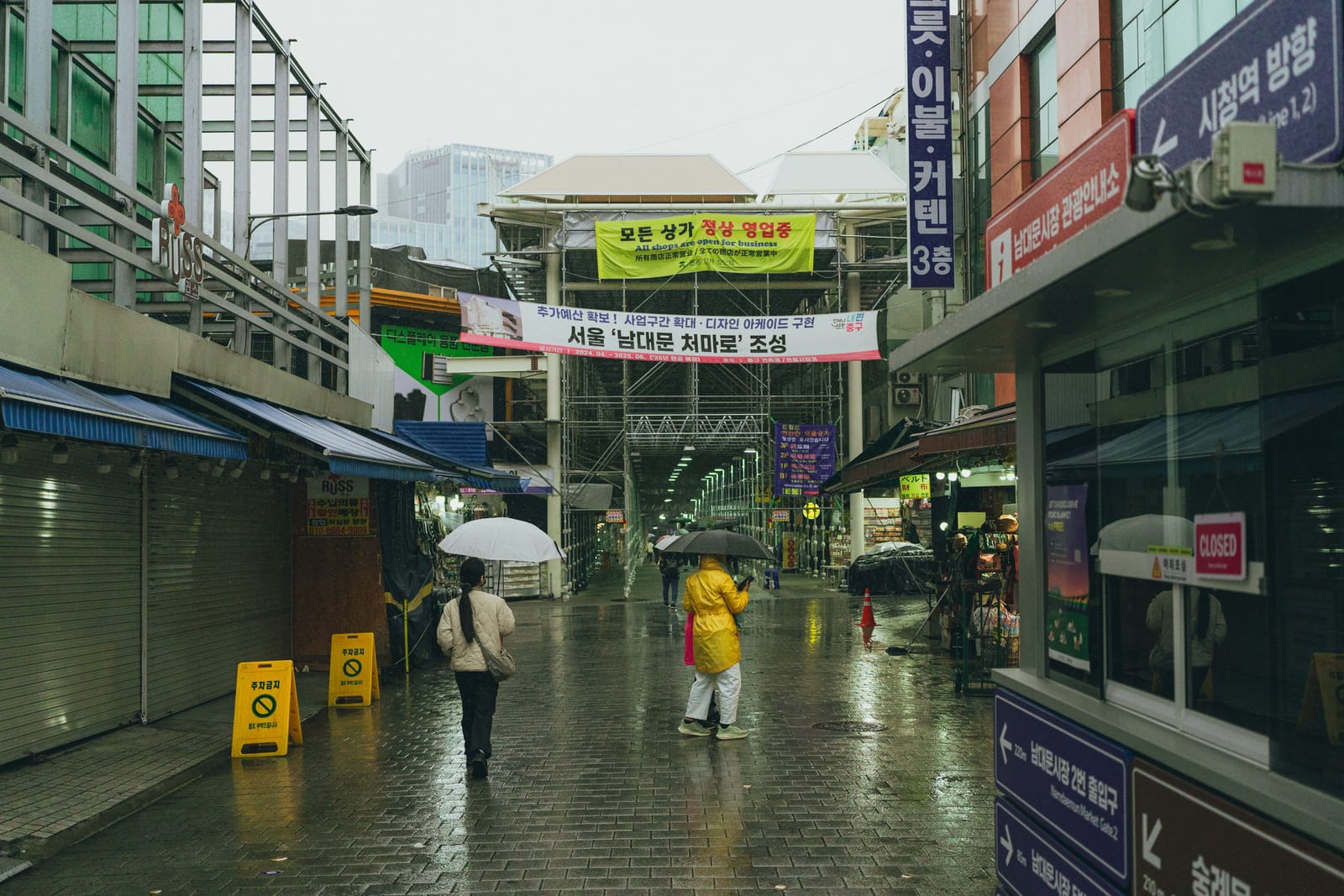 A person carrying a yellow umbrella through a rainy Seoul market street