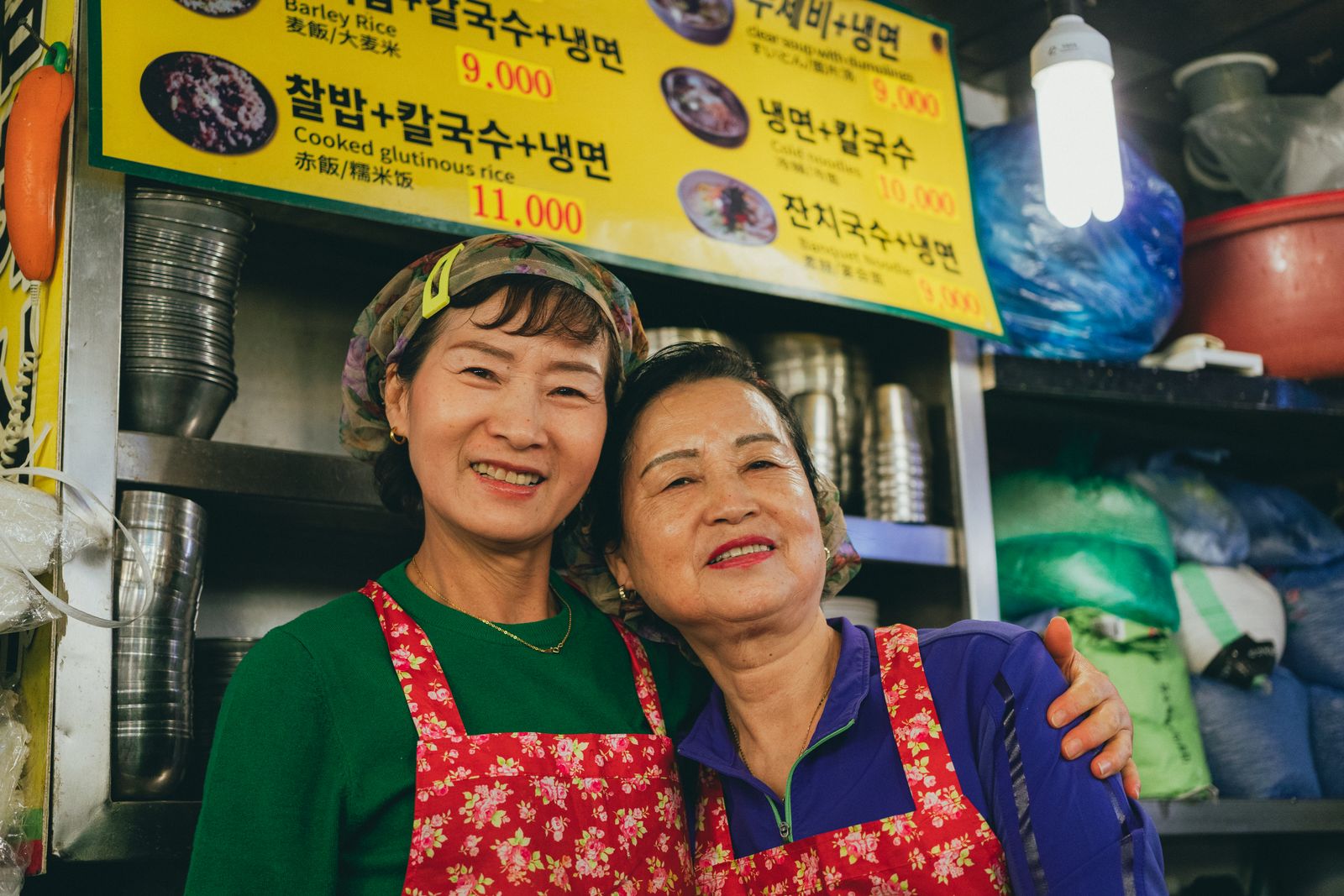 Two older women posing together at a Seoul market food stall