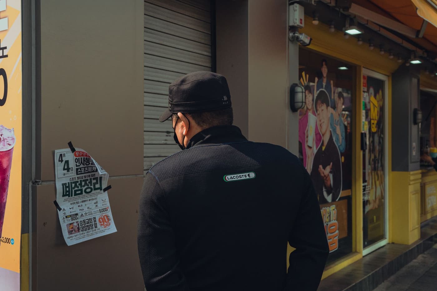 A pedestrian in Seoul reading posters on a city street, with layered urban signage behind.