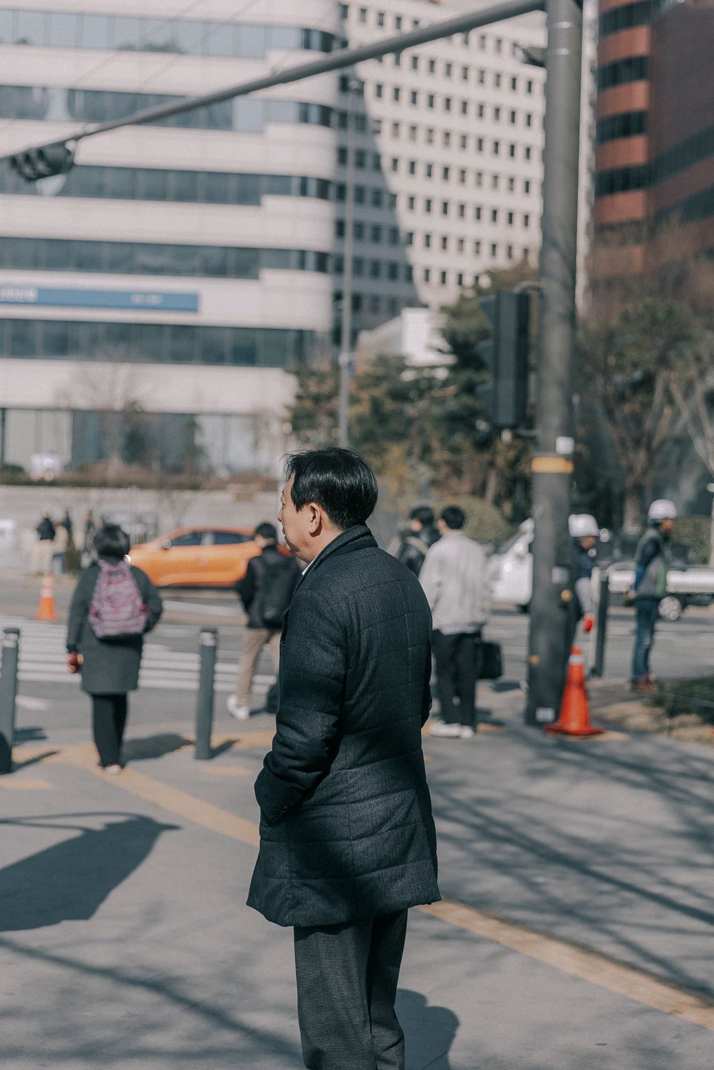 A commuter in a charcoal-black padded coat waiting at a Seoul crossing on a winter morning.