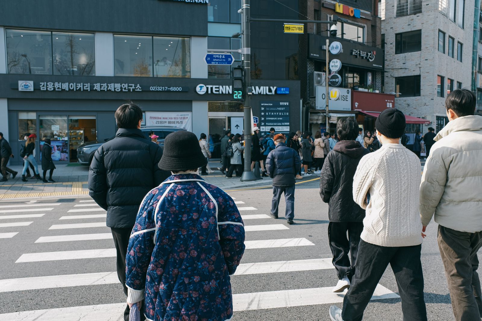 Pedestrians in padded winter jackets crossing a Seoul intersection with Korean shop signage.