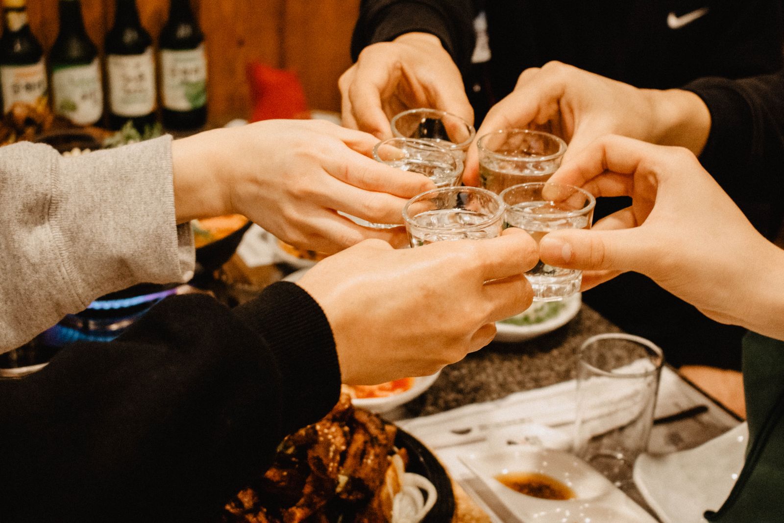 Friends toasting with soju glasses over a Korean restaurant table.