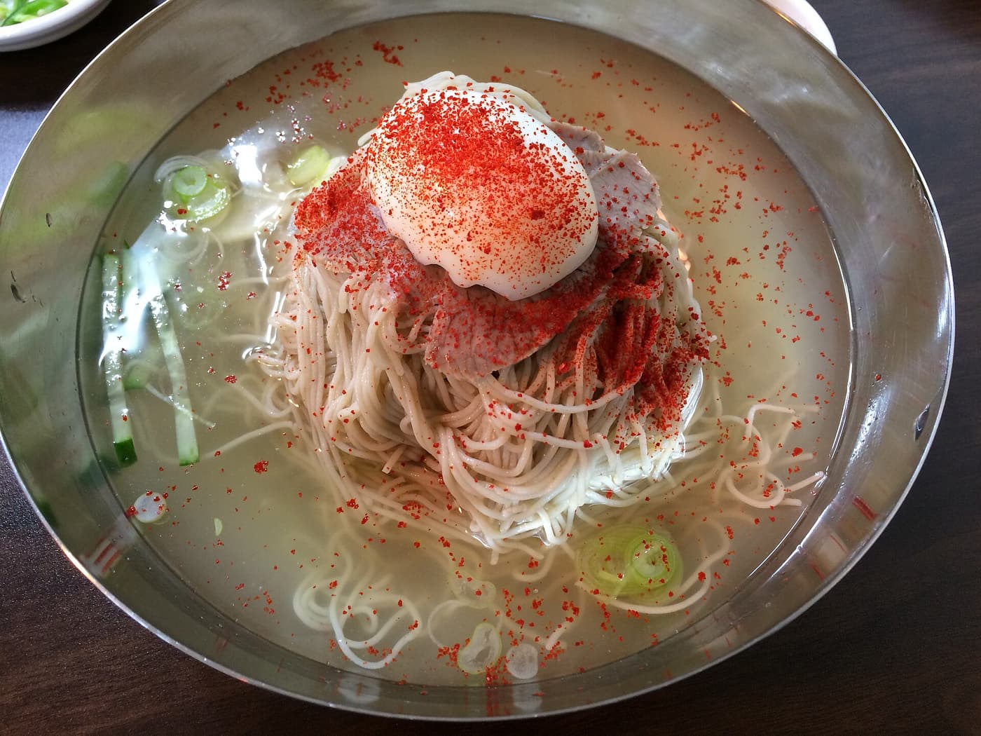 Naengmyeon served at a Korean restaurant table with garnishes and condiments.