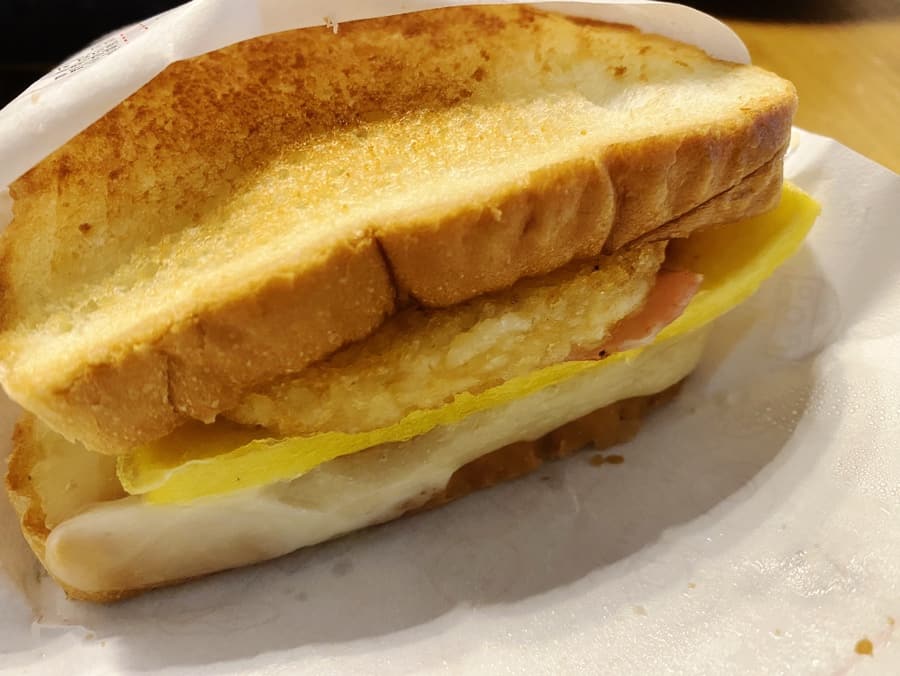 An Isaac Toast bacon potato pizza toast, cut open to show the filling between grilled slices of bread.