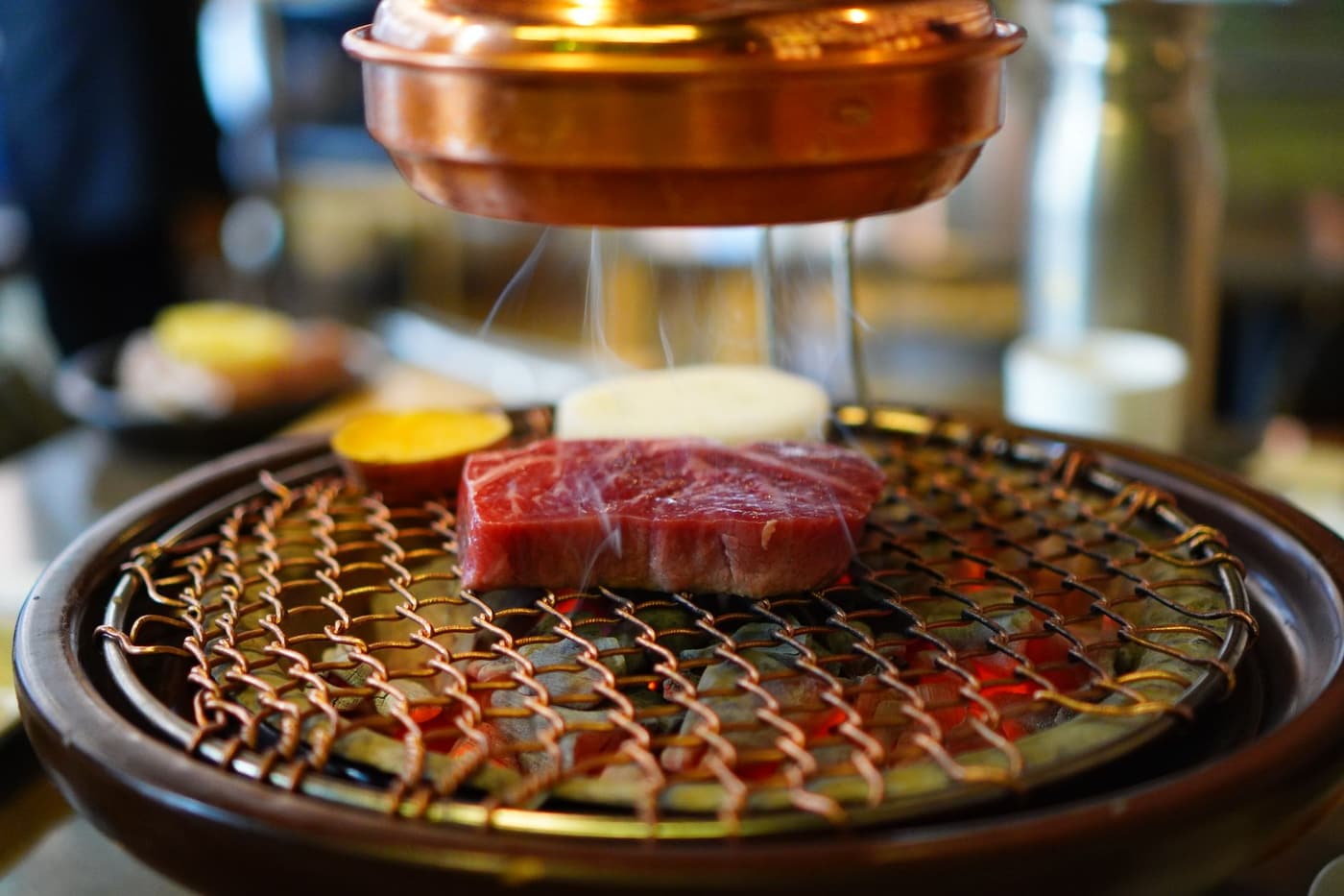 Close-up of raw beef on a Korean BBQ grill under a restaurant hood.