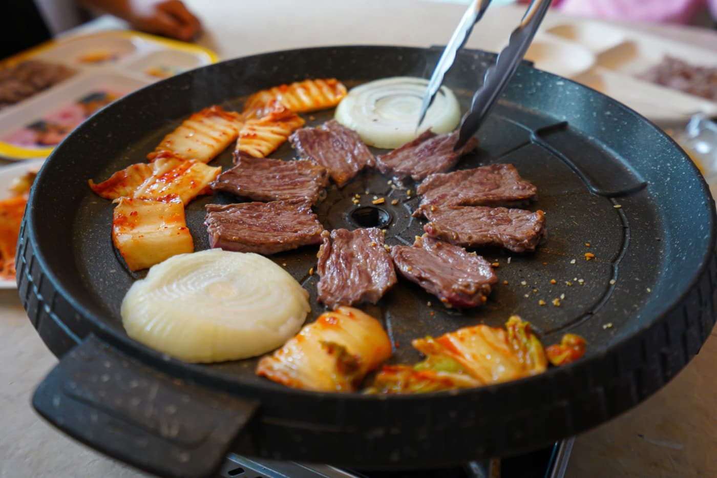Korean barbecue with grilled meat, onions, kimchi, and side dishes.