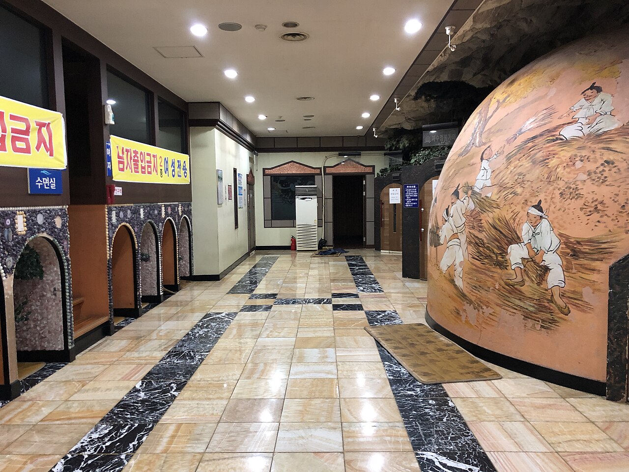 A Korean bulgama-style jjimjilbang room with warm-room doors, floor space, and Korean sauna signage.