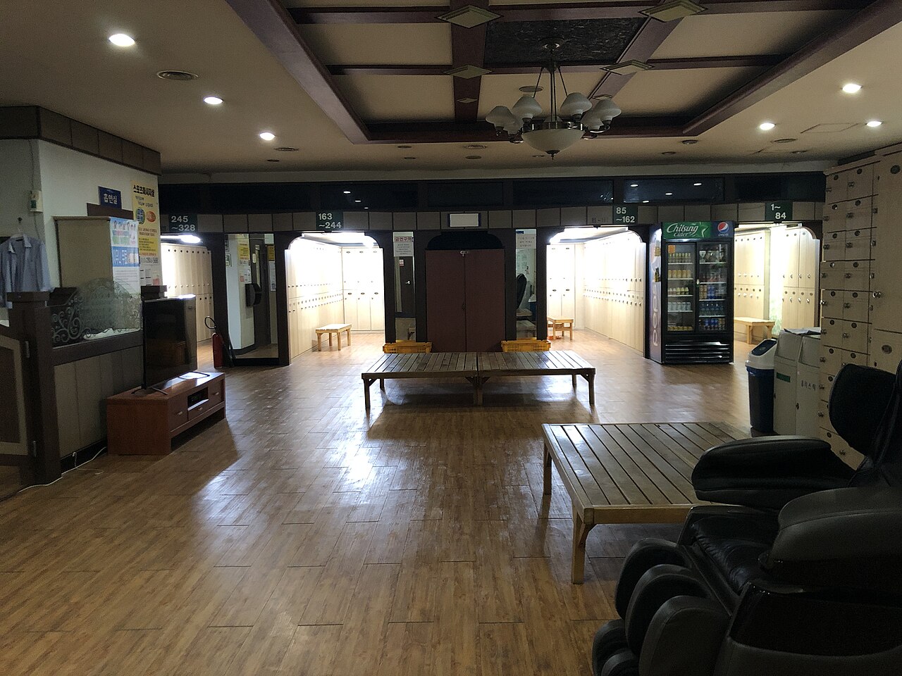 A Korean jjimjilbang common lounge with lockers, benches, drink machines, and resting space.