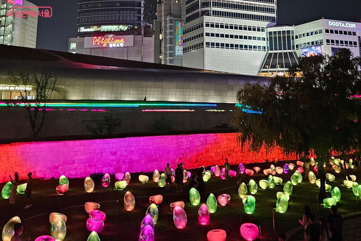 People walking through Seoul Light DDP on a hot summer night in Dongdaemun.