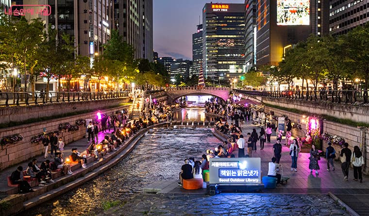 Crowds sitting along Cheonggyecheon during Seoul Outdoor Library's summer night program.