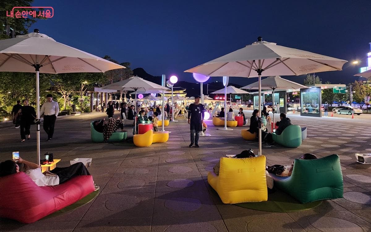 People relaxing outdoors at Gwanghwamun's Seoul Outdoor Library on a warm summer night.