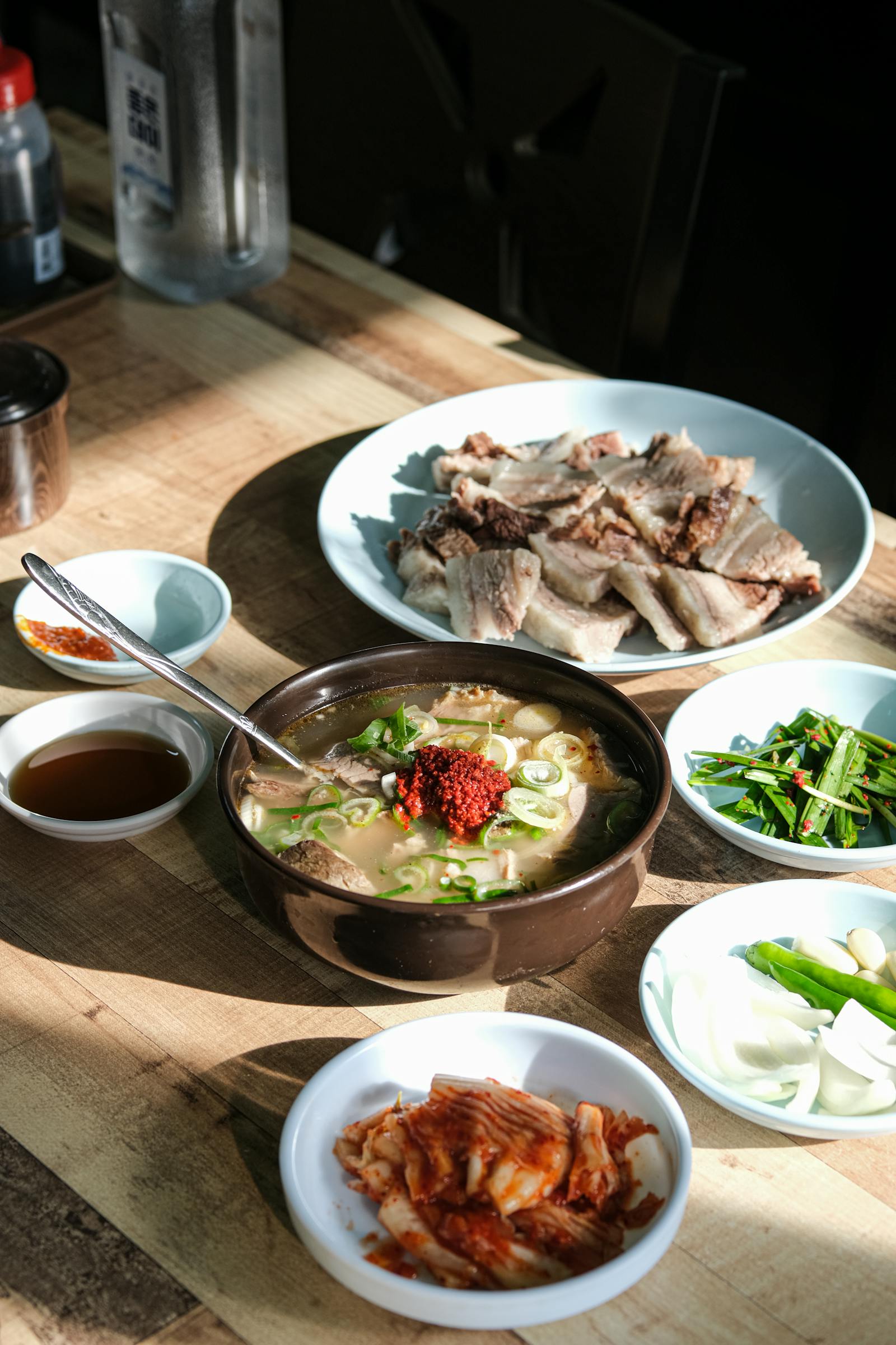A Korean soup-and-side-dish table with kimchi, pork, and banchan, showing the kind of complete meal structure solo diners often look for.