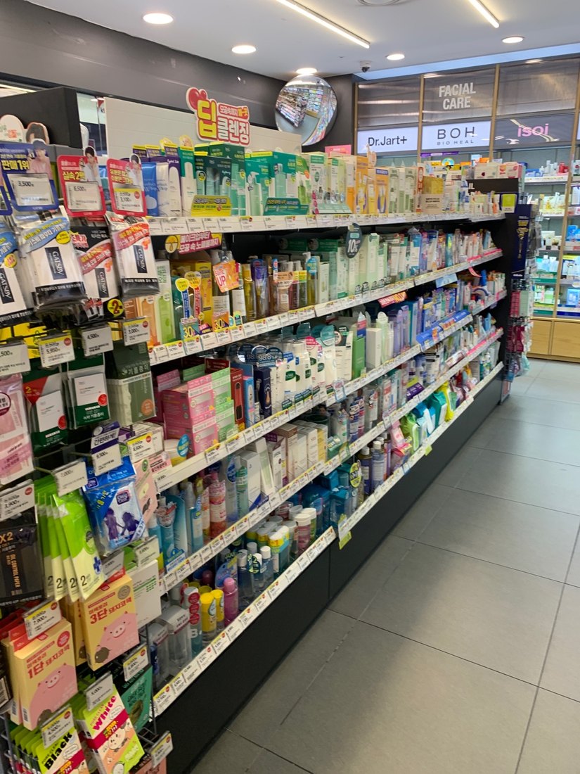 A skincare aisle inside an Olive Young branch: shelves of toners, serums and cleansers with Korean price tags and promotional flags, with Dr.Jart+, BOH and isoi brand signage on the facial-care wall behind.
