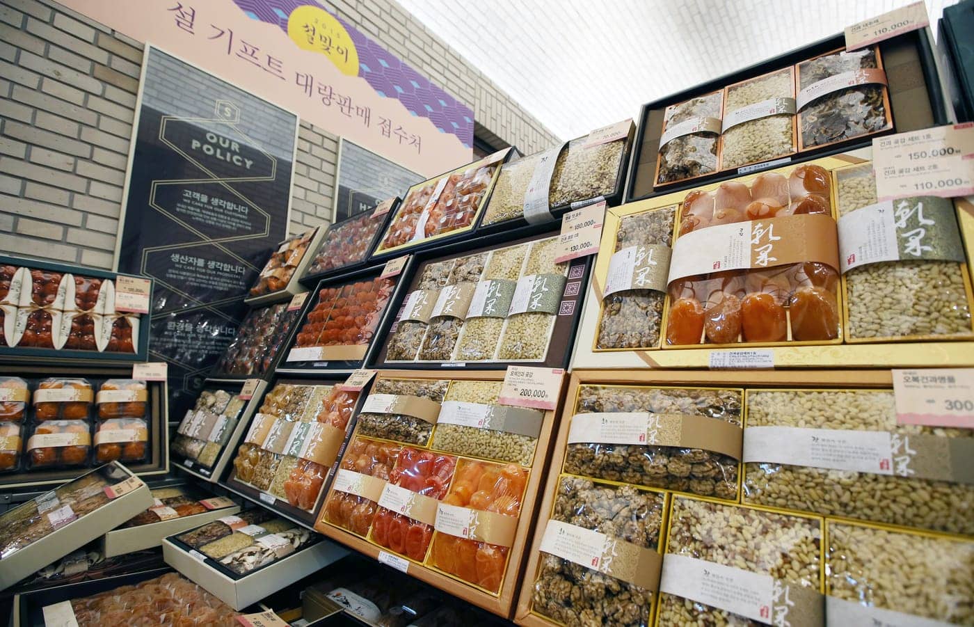 A wall of Korean holiday gift sets in a department store, boxed dried goods and hangwa stacked in tiers with price tags in the ₩110,000-300,000 range.