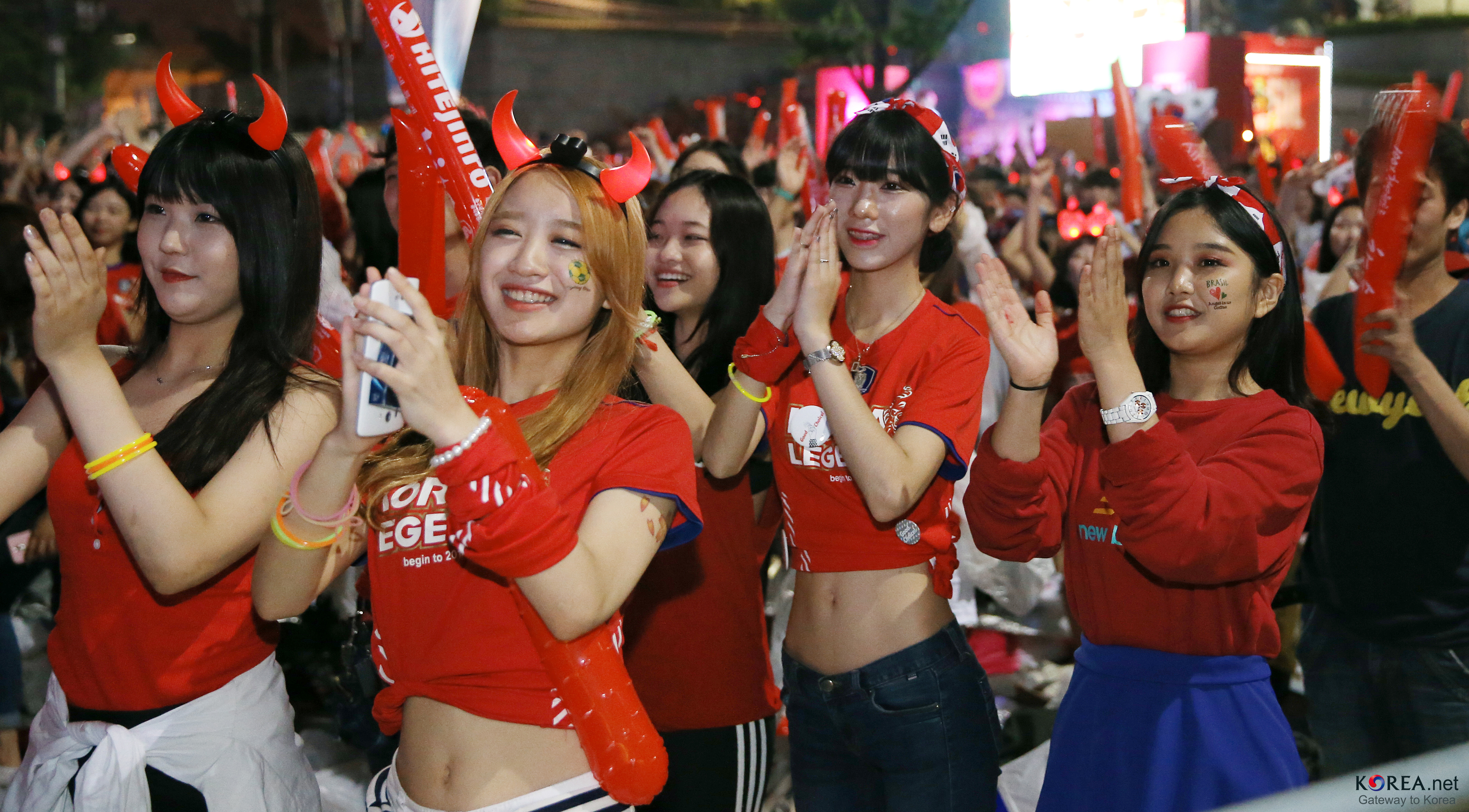 Korean football fans in red shirts and devil-horn headbands cheer in Gwanghwamun Square during a 2014 World Cup public viewing.