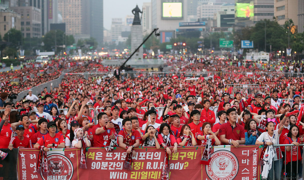 Korean football supporters holding cheering sticks and red accessories during a public viewing event.
