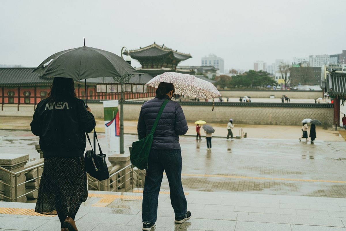 Visitors with umbrellas walking through Gyeongbokgung Palace on a rainy day.