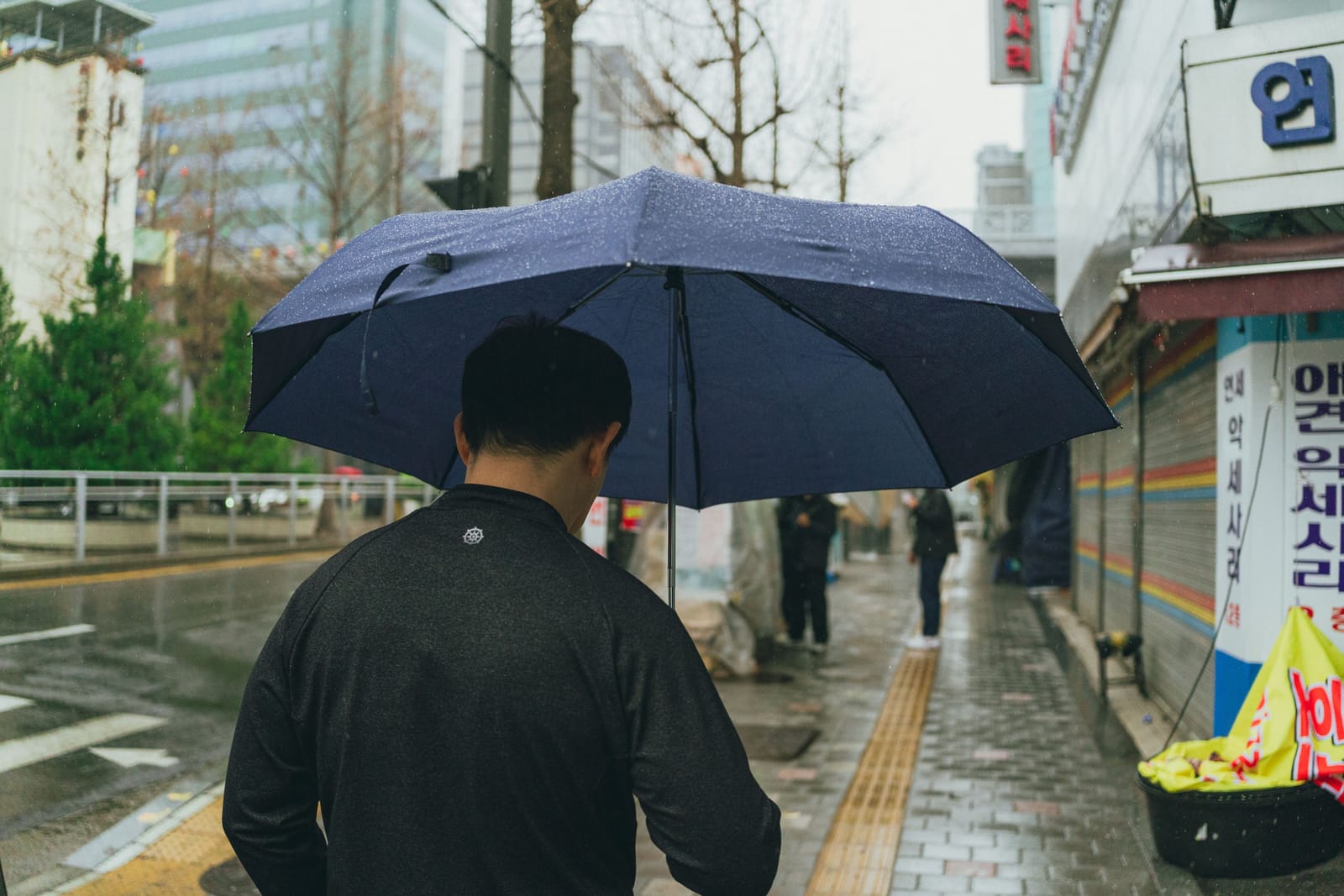 A rainy Seoul street with a pedestrian carrying an umbrella