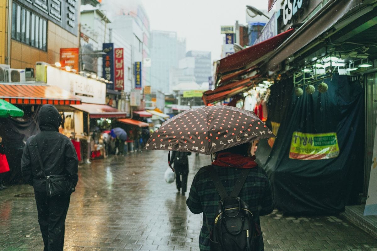 People carrying umbrellas through a rainy Seoul market street