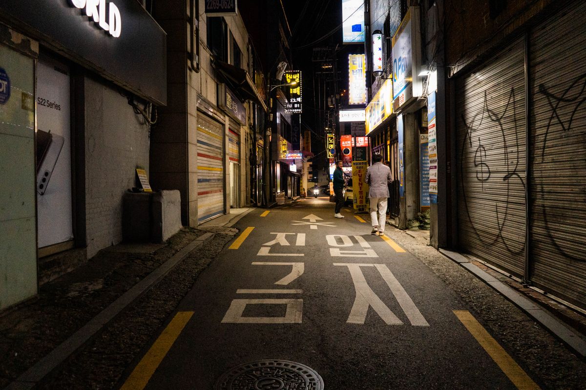 A narrow Seoul alley at night with Korean neon shop signs and a "no entry" road marking.