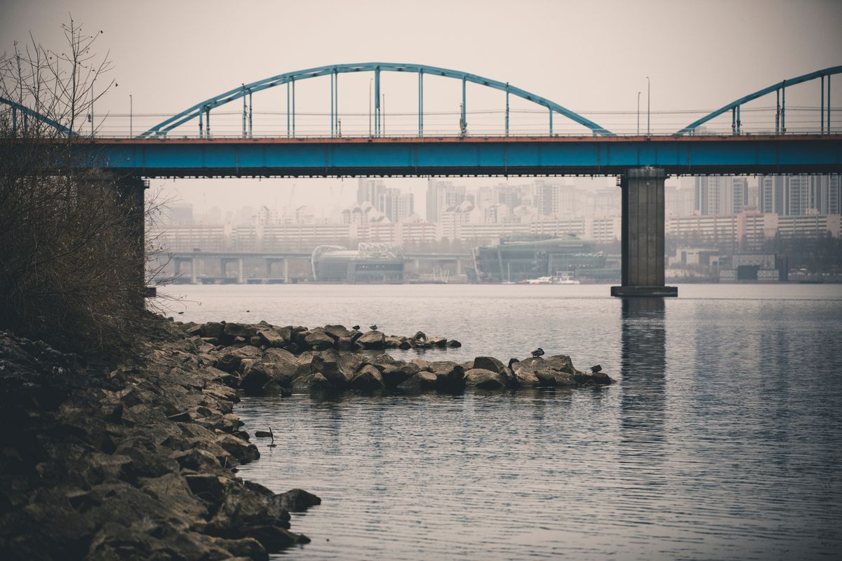 A blue bridge over the Han River with Seoul cityscape in the background.