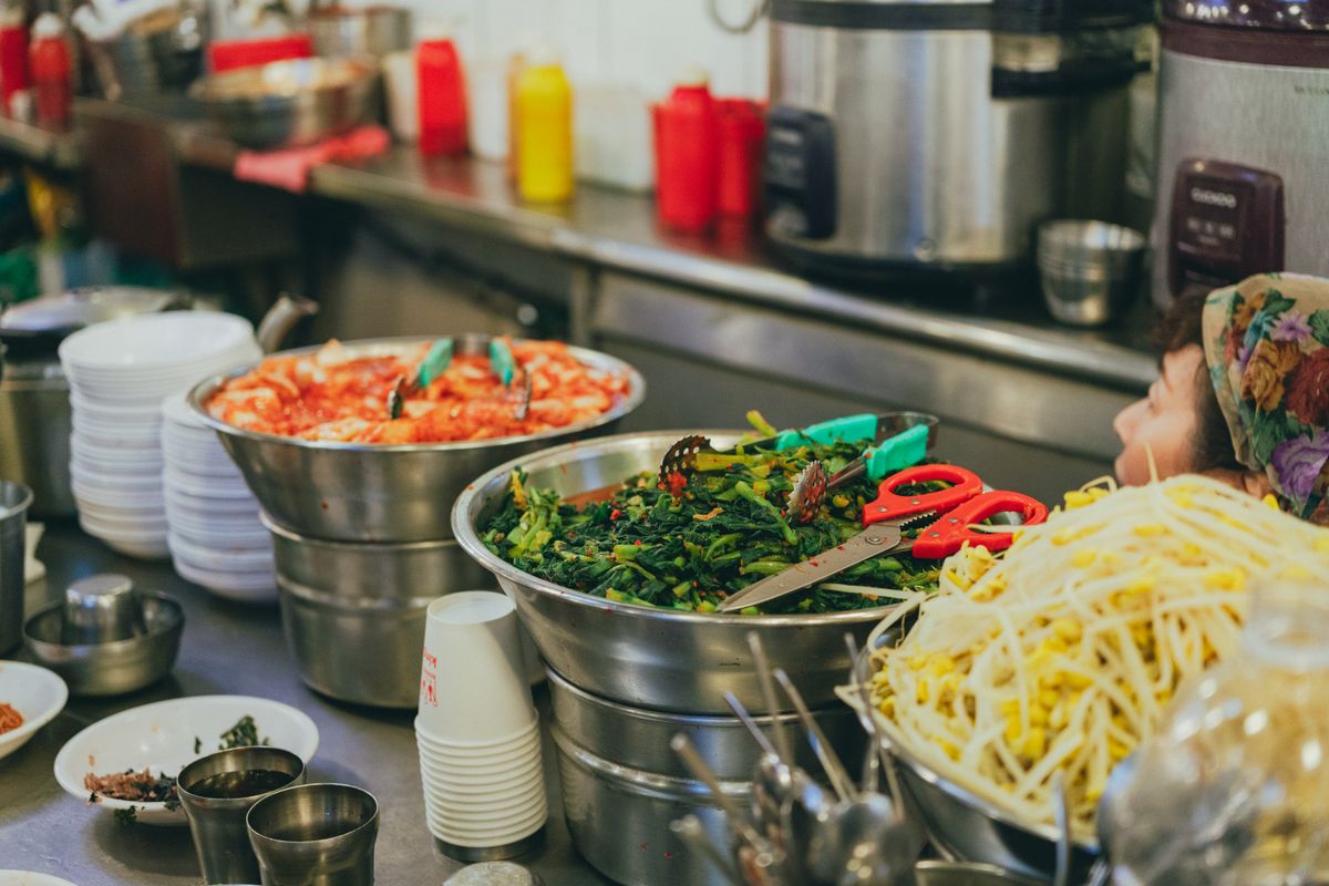 Prepared Korean market side dishes and vegetables arranged in metal bowls at a Seoul food stall.