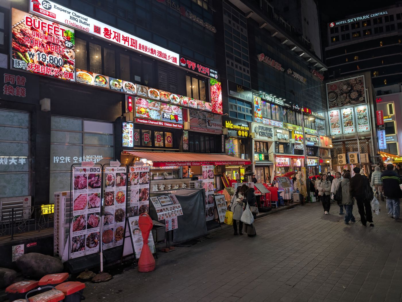A Seoul restaurant street at night with many signs and options.