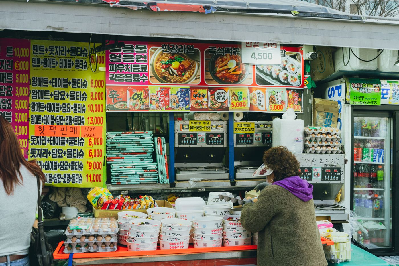 A Korean street-food stall with ramen and tteokbokki packaging, showing why menu boards and packaged ingredients can overlap.