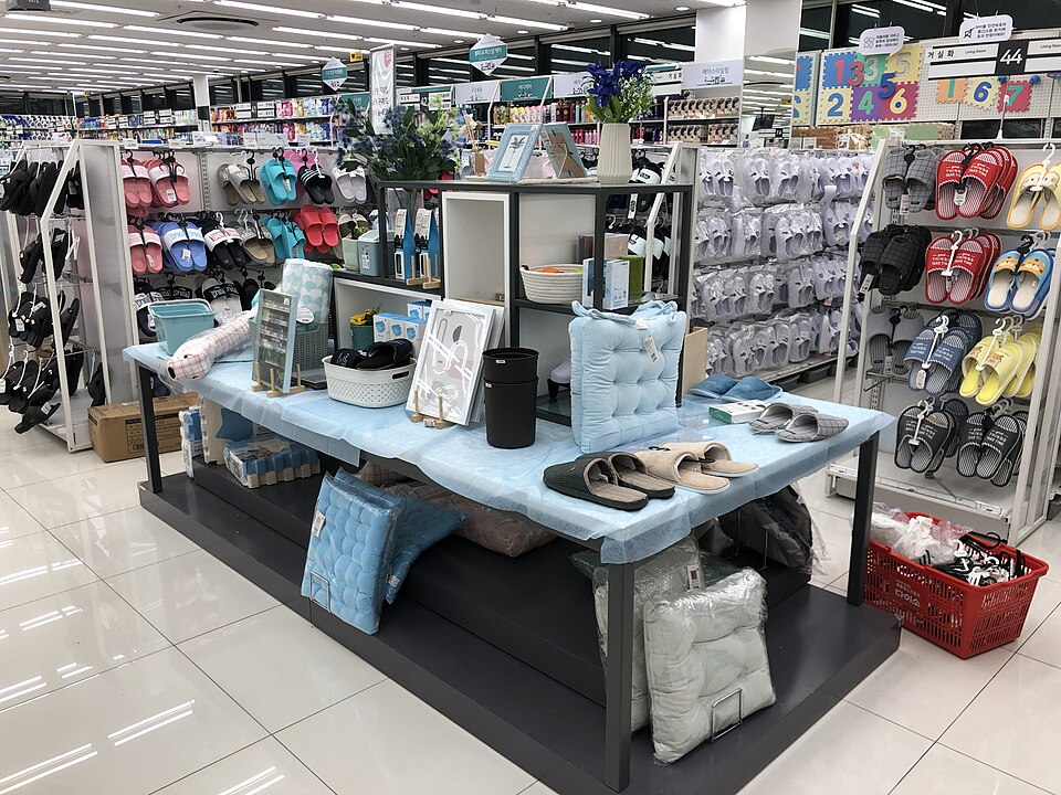 A home goods display inside Daiso Wonju Musil with slippers, cushions, and small comfort items arranged under Korean aisle signs.