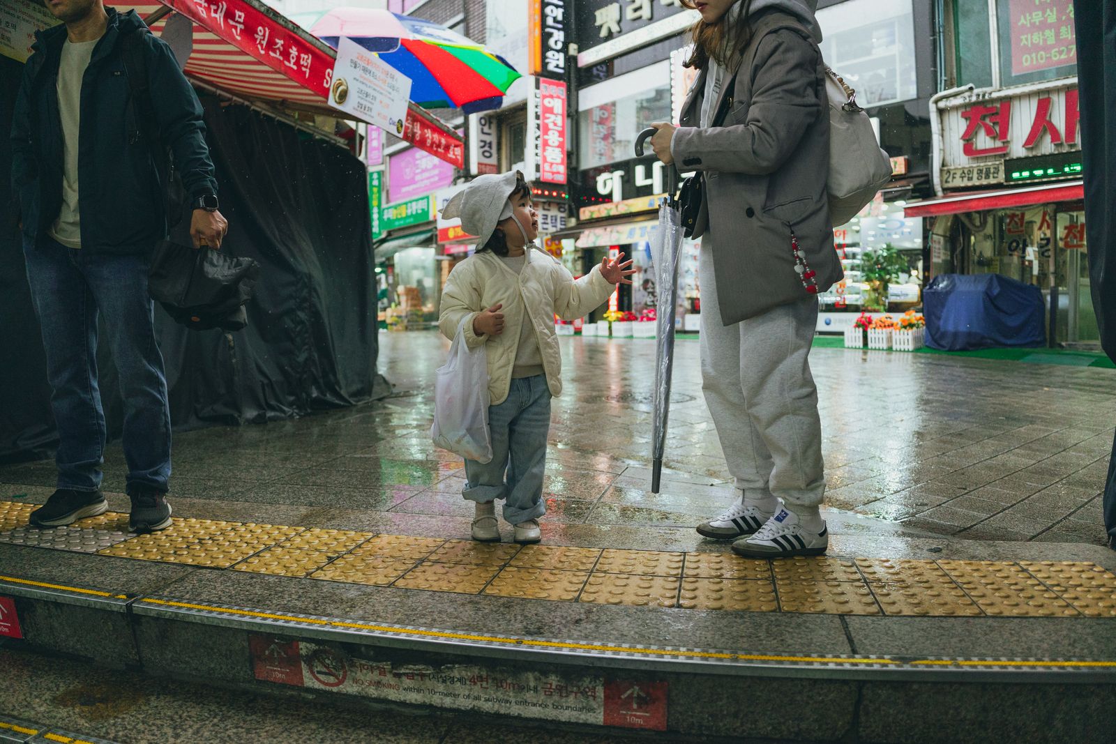 A family navigating a rainy Seoul street with umbrellas, showing why one indoor cultural stop should carry the afternoon instead of too many wet transfers.